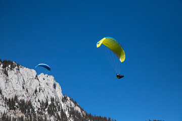 gelber gleitschirm unter blauem Himmel, Pilot in Wärmesack im Gleitflug bei sonnigem Frühling am...