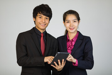 Asian man and woman businesspeople in formal suit standing together and holding tablet computer and smile to camera with self-confidence