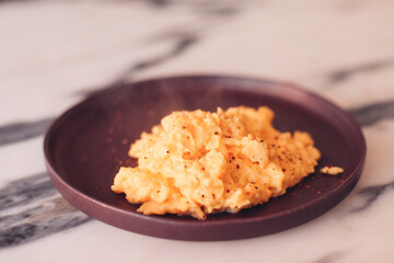 Creamy omelet, scrambled eggs on a purple plate on a marble background