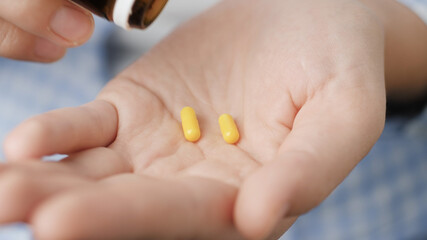 Two small bright yellow cylindrical pill capsules fall into palm of hand from pill bottle. Close-up, front view, center composition