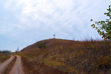 Beautiful autumn landscape. Hill view with orthodox cross and road on blue cloudy sky background