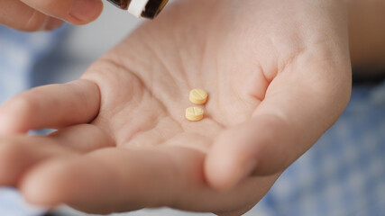 Two small yellow round pills fall into palm of hand from pill bottle. Close-up, front view, center composition