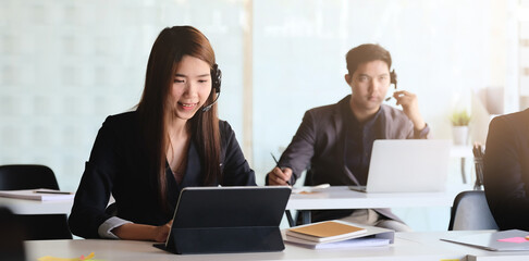 Young asian woman working in call centre, surrounded by colleagues.