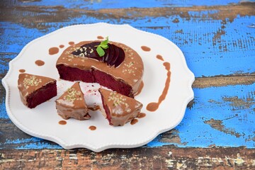 Homemade gluten free vegan beetroot chocolate cake with almond butter topping garnish with hemp seeds, mint leaf and sliced beetroot. Blue wooden background © AmalliaEka