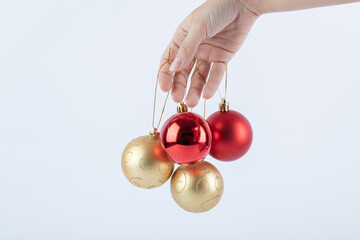 Female hand holding shiny Christmas baubles on white background