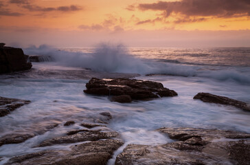 Obraz premium Coastal sunrise waves crashing onto rocks