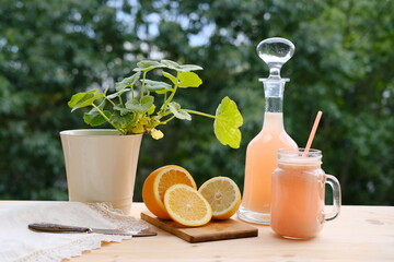 fresh fruit smoothies in a decanter and a mug on a background of green garden foliage, orange...