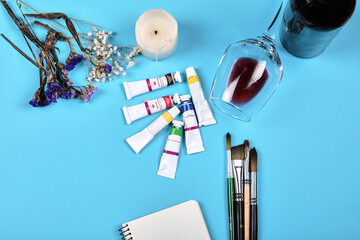 Colorful oil painting tubes, paintbrushes, candle and a glass of wine