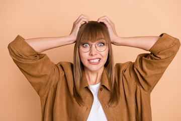 Photo of worried guilty young woman hold hands head wear glasses mistake afraid isolated on beige color background