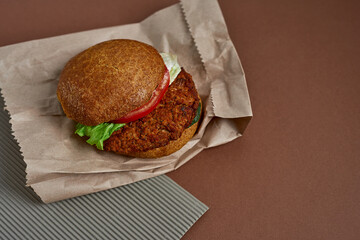 Vegetarian burger made rolled oats, chick peas, crushed onions and garlic, tomatoes, spices on a whole wheat bun and salat on the paper bag. Copy space. Healthy food concept.