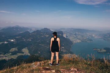 young girl of European descent and in sportswear stands on the edge of the Schafberg rock in...