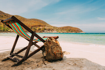 open sea, A deck chair on the sandy shore of a tropical beach. stylish brown backpack standing nearby. traveler, freelancer