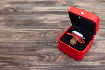 Baby pacifier in red gift box on wooden background