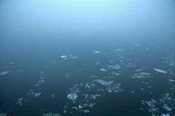Fototapeta premium Misty icy blue water surface with endless fog on river Danube; color photo.