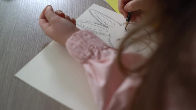 close-up of a girl's hand sitting at the table and drawing a portrait of a hare. happy easter concept.
