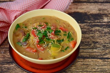 Gluten free chickpea noodles soup with spinach, red bell pepper and bok choy garnish with parsley and sesame seeds
