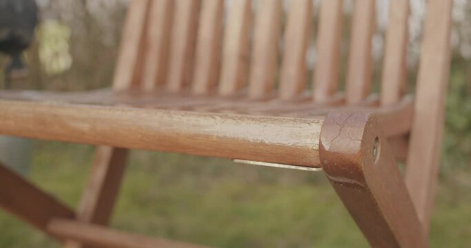 Close up shot putting linseed oil onto a wooden outdoor chair after the winter. Handheld close up shot with shallow depth of field. Gloves handling a brush in the background.