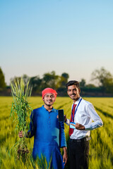 Young indian agronomist with farmer at green wheat field