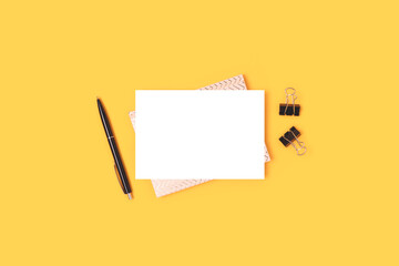 Empty paper card mockup and black stationery on a yellow background. Minimalistic business workspace.