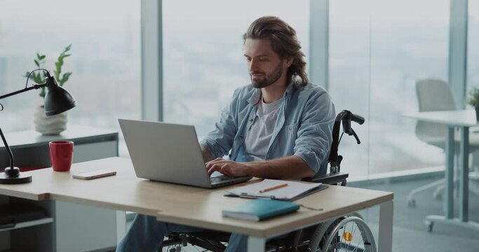 Young attractive business manager worker in wheelkchair doing work in corporate workspace. Office employee. Person with disabilities.