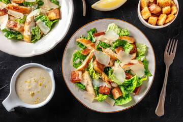 Caesar salad with chicken, green leaves and Parmesan, shot from above with the classic sauce on a black background