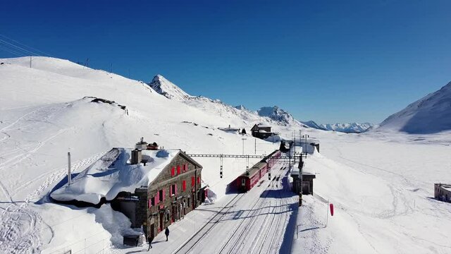 Switzerland Alps , Poschiavo - drone view of  Bernina Express, red train of Bernina pass in Ospizio Bernina station -  Unesco world heritage - White lake ( lago bianco ) frozen 
