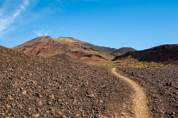 Path in desert and silhouette of volcano del Teide against  blue sky and female hiker with backpack. Pico del Teide mountain in El Teide National park. Tenerife, Canary Islands, Spain