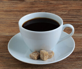 White porcelain cup and saucer with coffee and cane brown sugar on wooden table. Close-up