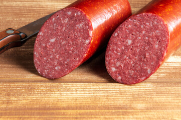 Sliced salami sausage and knife on cutting board closeup. Food preparation idea before the holiday