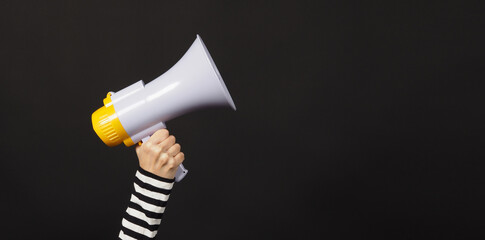 woman's hands is holding megaphone on black background.woman wear black and white stripe t shirt.