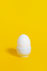 White chicken egg in white ceramic tray on bright, saturated yellow background. Easter breakfast concept. Copy space. Organic product, meal, food.