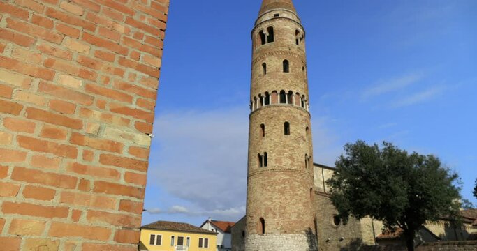 Bell tower campanile on the Duomo square with a pair walking and azure sky Caorle Italy