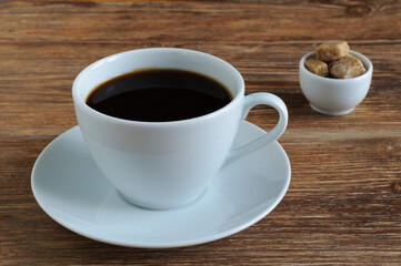 Fototapeta na wymiar White porcelain cup and saucer with black coffee and cane brown sugar on wooden table