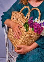 Woman holding hands wicker bag with lilac flowers indoor, Sitting on a vintage chair