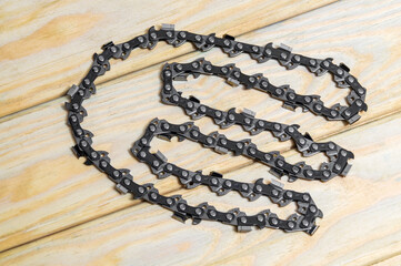 Obraz na płótnie Canvas Metal chain for the brushcutter is laid out on the wooden table before installation or replacement. Suitable for cutting brows or trees