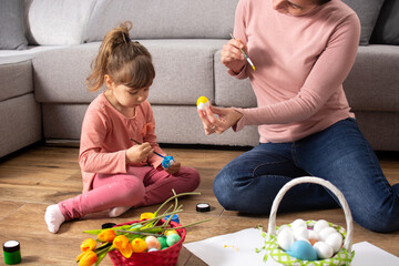 Naklejka premium A mother and her daughter painting Easter eggs at home.