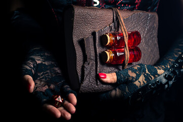 Women wearing black lace gloves holding a brown leather bound tome with glass bottles containing...
