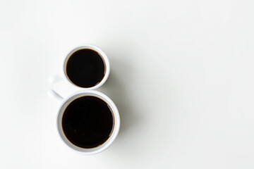 Two cups of black coffee are in the shape of an eight on the white table