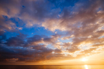 Naklejka na ściany i meble Calm sea with sunset sky and sun through the clouds over.
