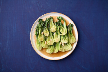 Stir fried bok choy with soy sauce on plate with blue background, Asian vegan food, Top view