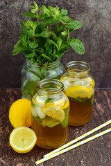 Iced lemon tea with lemon slices and mint leaves and ice cubes on rustic background