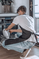 handsome young man sitting near an open dishwasher