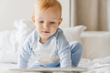 Fototapeta premium Focused blonde baby boy looking at tablet computer while playing on bed
