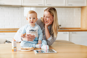 Happy beautiful woman using tablet computer while feeding her baby son