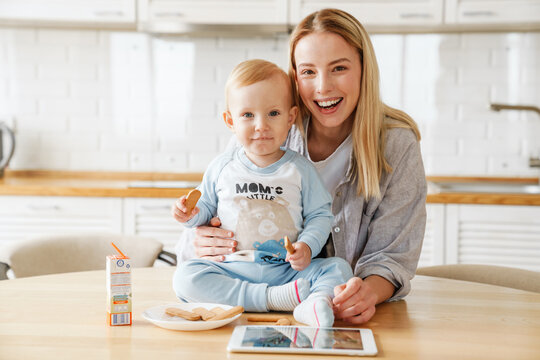 Happy beautiful woman using tablet computer while feeding her baby son