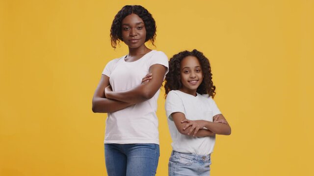 Confident black mother and daughter standing back to back with folded arms, looking at each other and nodding heads
