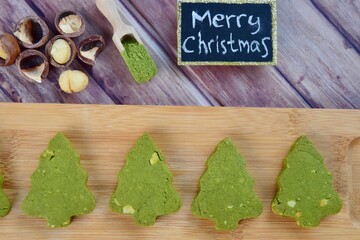 Green tea Matcha Christmas tree cookies with Macadamia on wood background. Merry Christmas letter writing on black board.