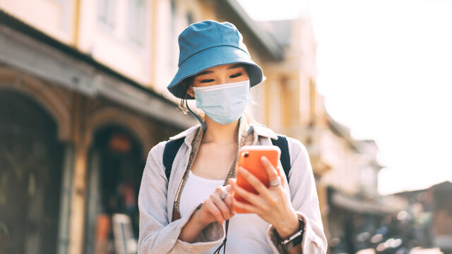 Young Adult Asian Woman Backpack Traveller Wear Face Mask And Using Mobile Phone For Application.