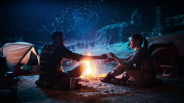 Happy Couple Nature Camping in the Canyon Together, Sitting by Campfire Sharing Cup of Drink, Night Sky Watching