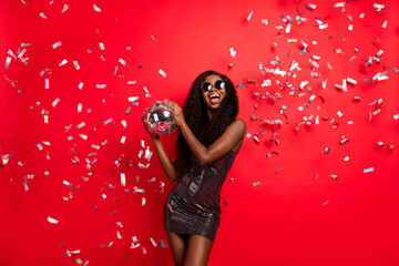Photo of young african girl happy smile hold disco ball party fly air confetti isolated over red...